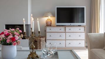 Un salon avec un meuble TV blanc, un canapé blanc, une table basse ornée d’un vase de fleurs et une cheminée.