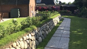 Ein Haus mit einem Strohdach, einem Steinweg und einem Garten mit blühenden Pflanzen.
