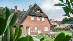 Ein Backsteinhaus mit Strohdach, einer weißen Tür und einem kleinen Garten mit einem Weg zum Eingang.