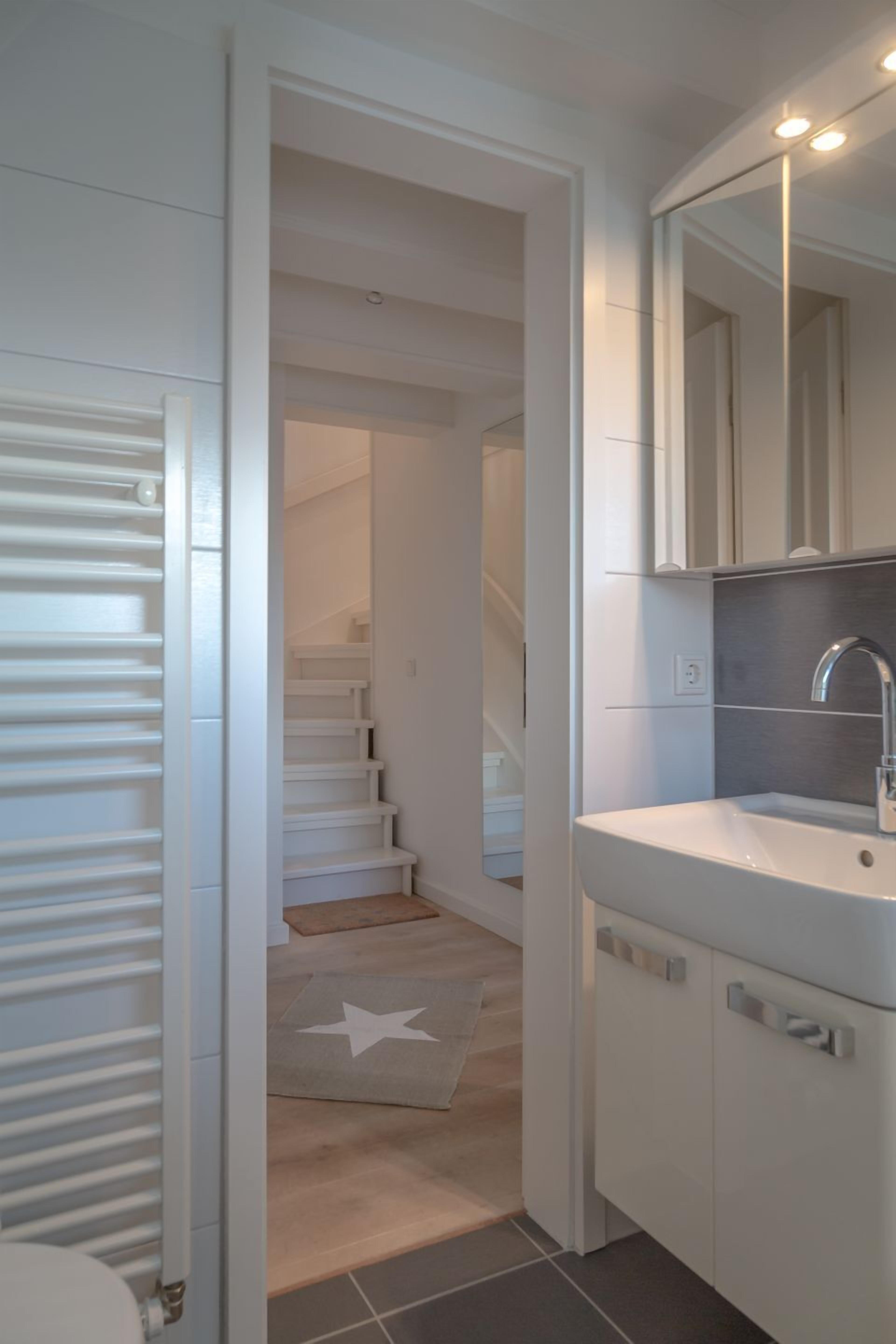 Un baño moderno con un lavamanos blanco, espejo y una escalera que lleva a otra habitación.