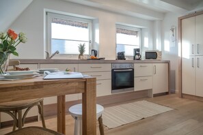 Une cuisine moderne équipée d’un four encastré, d’un four à micro-ondes et d’une machine à café. On y trouve une table à manger avec des chaises, ainsi qu’une petite table ronde.