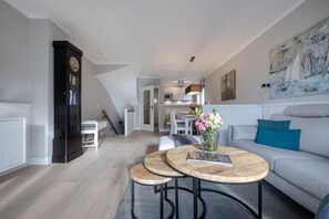 Una sala de estar moderna con un sofá gris, dos mesas redondas de madera, un reloj y un cuadro en la pared.
