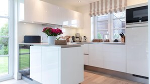 Een moderne keuken met witte kasten, een inbouw eiland en een groot raam met strepen gordijnen.
