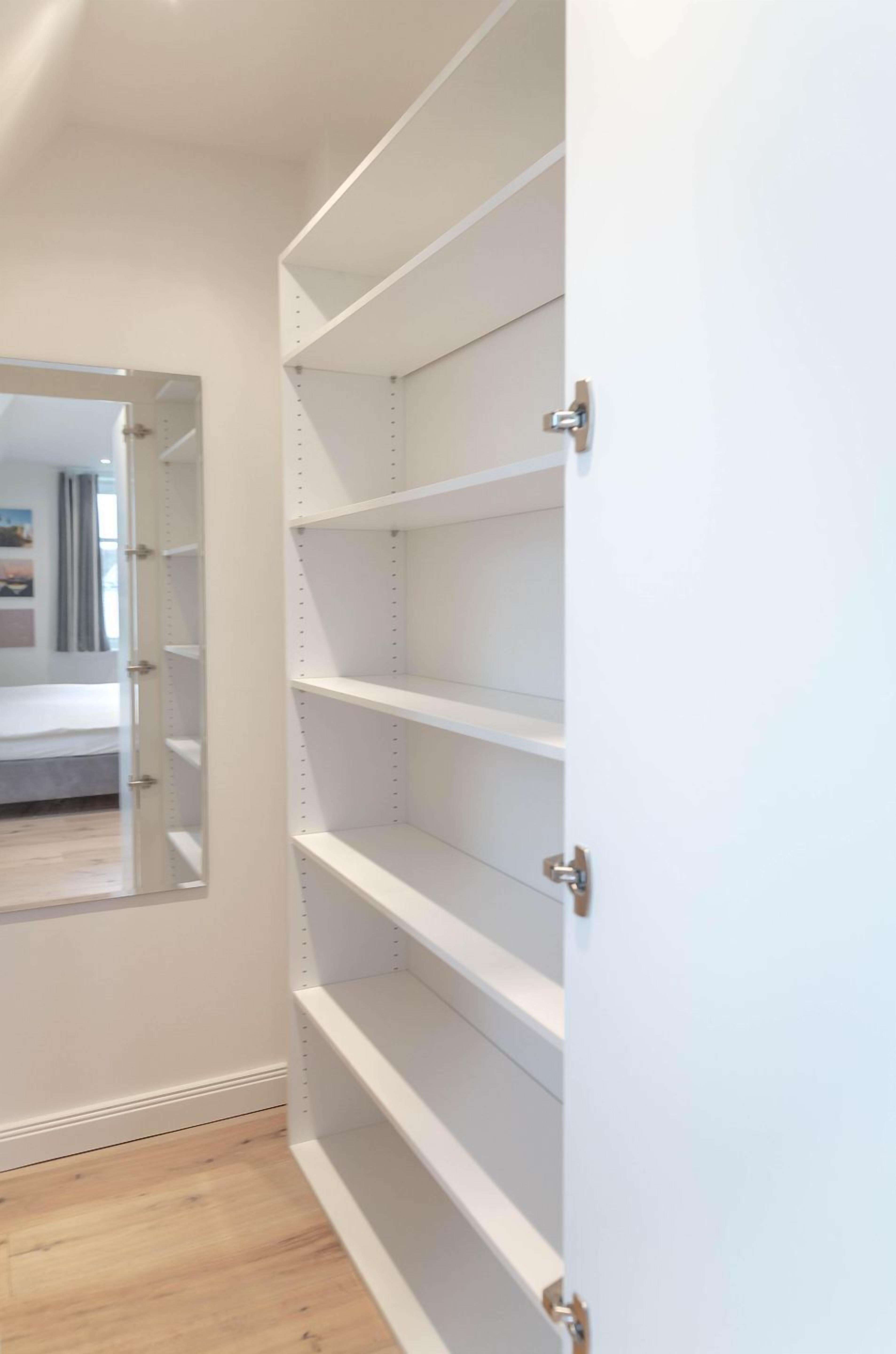 A hallway with white shelving units and a door leading to a bedroom.