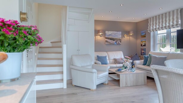 Een moderne woonkamer met een trap, witte banken, een salontafel en een groot raam met gordijnen.
