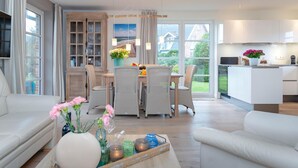 Een moderne woonkamer met een eethoek, een keuken en grote ramen met uitzicht op het groen.