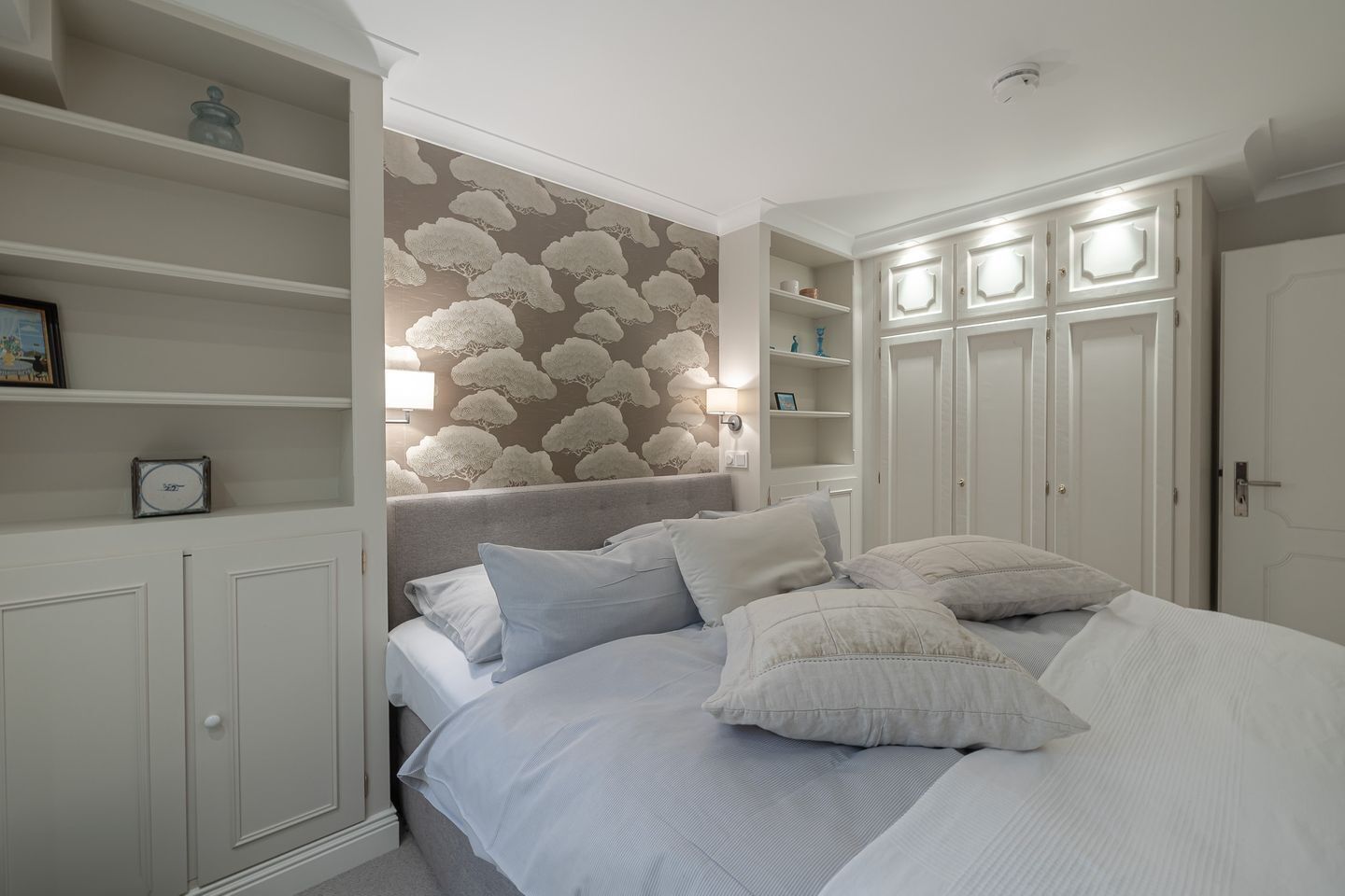 Een slaapkamer met een bed, nachtkastjes, een kledingkast en een wand met een wolkenprint.