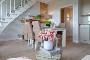Un comedor con una mesa lista para dos personas, rodeada de sillas, una escalera y una zona de cocina.