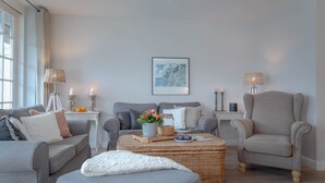 Un salon moderne avec des canapés gris, une table basse ronde et deux fauteuils. On trouve des objets décoratifs sur la table basse, et un tableau au mur.