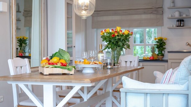 Un coin repas avec une table en bois, des chaises blanches et un vase rempli de roses jaunes.