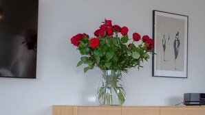 Un salon avec un meuble en bois, un fauteuil vert, un vase de roses rouges et un panier de fruits posé sur une table basse.