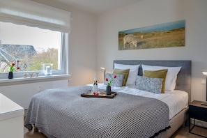 Un dormitorio ordenado con una cama grande, una mesita de noche, una ventana con vistas al exterior y un cuadro en la pared.