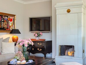 A living room with a sofa, a coffee table with pastries, a TV, a fireplace, and a decorative painting.