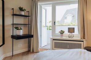 Un dormitorio con cama, ventana con cortinas, radiador y dos estantes con plantas.