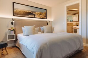 Un dormitorio moderno con una cama grande, una mesita de noche con un florero y un cuadro colgado en la pared.