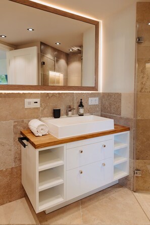 Un baño moderno con un tocador blanco, un espejo grande y una zona de ducha.