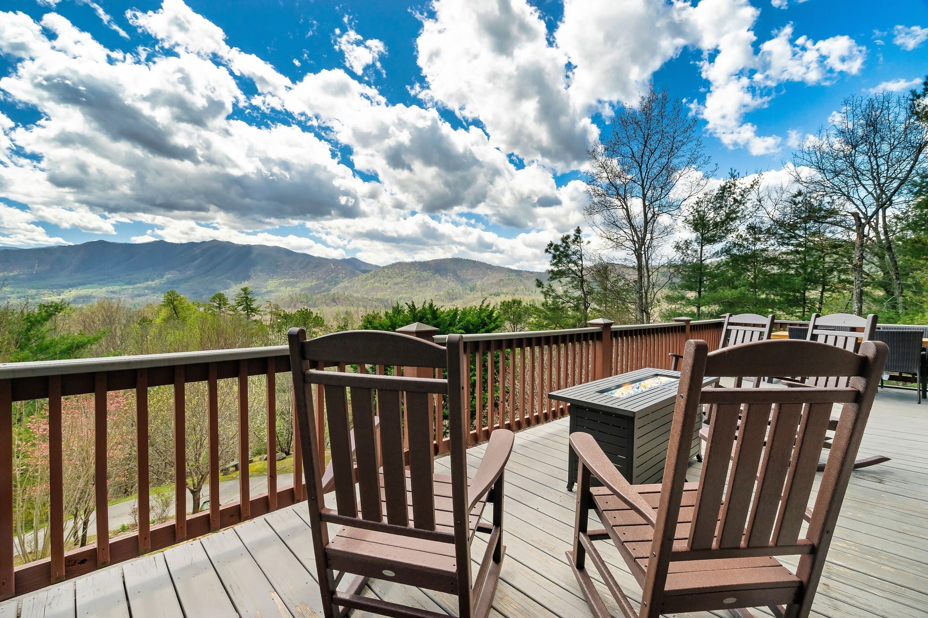 Terraza de madera con sillas y una mesa, con vistas a un paisaje montañoso.