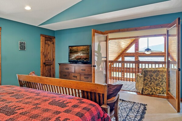 A bedroom with a bed, a dresser, a painting, and a balcony with a chair. - VIEWS! Spacious and relaxing cabin! VIEWS! (Townsend)