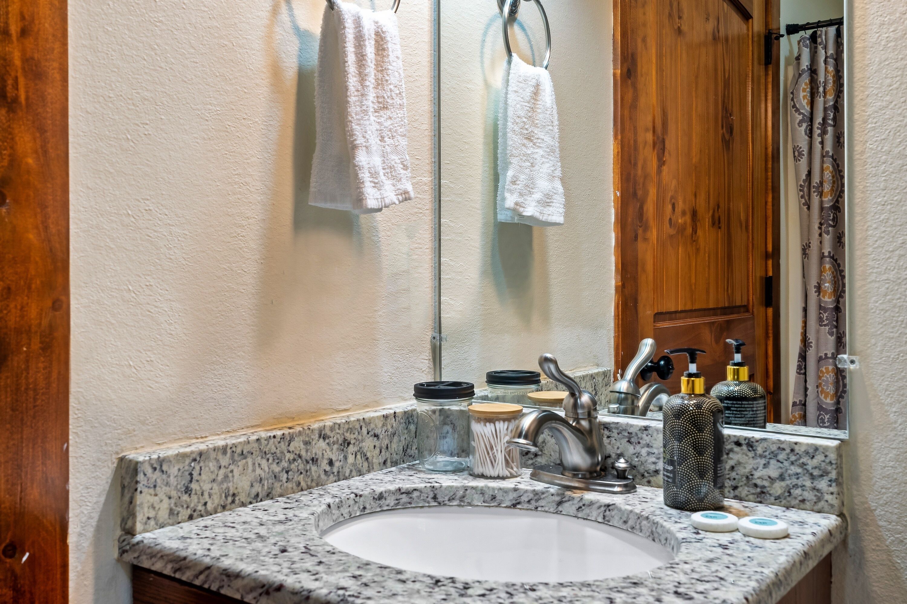 Une salle de bain avec un lavabo doté d’un plan de travail en granit, un miroir et une porte en bois.