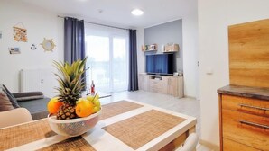 A modern living room with a dining table, a fruit bowl, and a TV in the background. - Apartment A 204 by Interhome (Kolobrzeg)