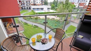 A balcony with wicker chairs, a glass table with fruit and drinks, and a view of a residential area with buildings and greenery. - Apartment A 204 by Interhome (Kolobrzeg)
