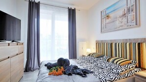 A modern hotel room with a large bed, a flat-screen TV, a painting on the wall, and a window with curtains. - Apartment A 204 by Interhome (Kolobrzeg)