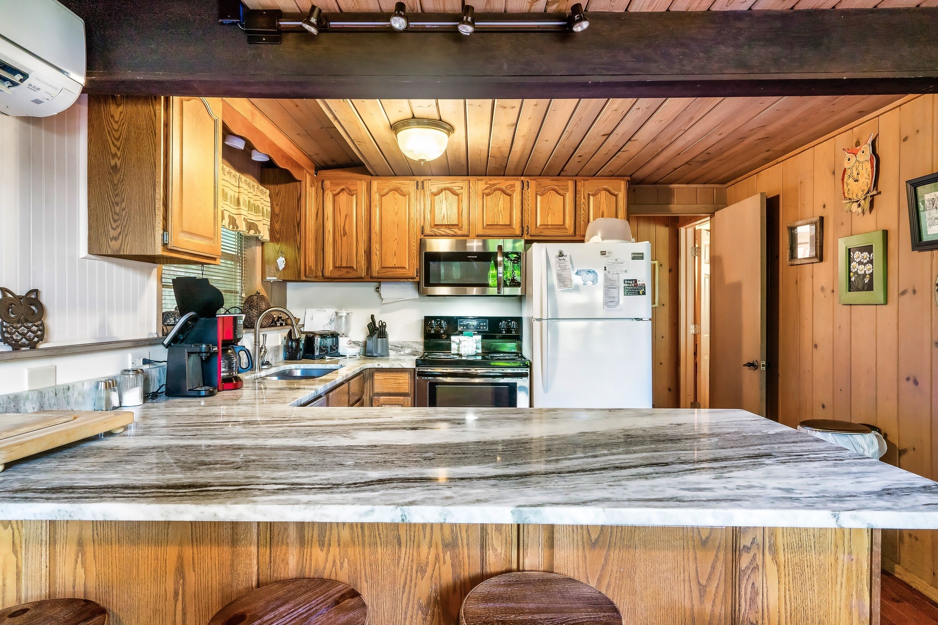 Una cocina con armarios de madera, encimera de mármol, microondas, estufa y refrigerador.