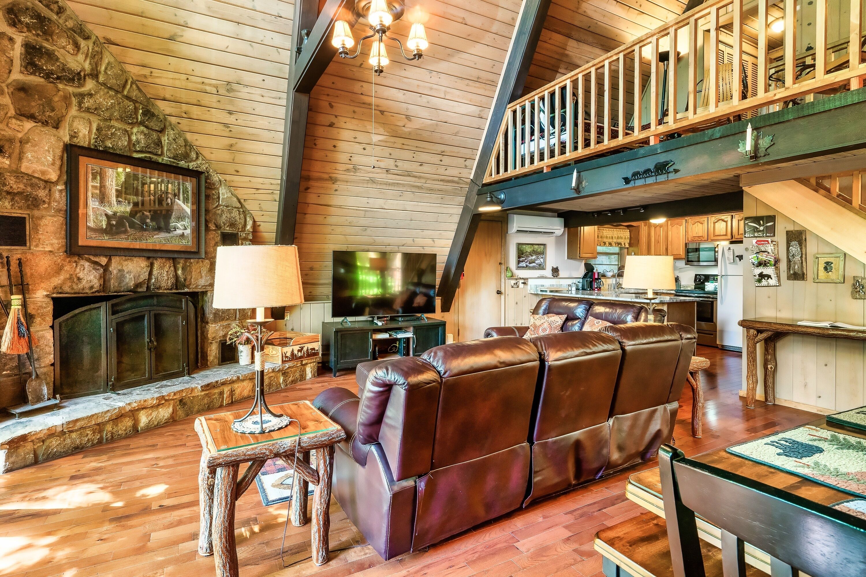A spacious living area with a stone fireplace, leather sofa, wooden flooring, and a balcony.