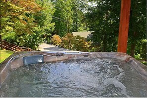 A hot tub with a wooden deck and a view of a residential area with trees and a house.