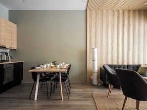 A modern kitchen with a dining area, featuring a wooden table set for four, black chairs, and a black sofa with a woven rug.