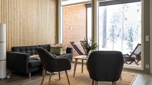 Una sala moderna con un sofá oscuro, dos sillones, una mesita y un ventanal con vistas a un paisaje nevado.