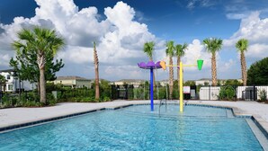 Une piscine agrémentée d’un élément décoratif aquatique, entourée de palmiers et d’une clôture.