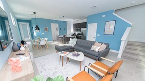 Un salon moderne avec un canapé d’angle gris, une table basse et un coin repas comprenant une table et des chaises blanches.