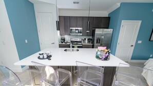 Une cuisine moderne dotée d’un îlot central, d’appareils électroménagers en acier inoxydable et de chaises en plastique transparent.