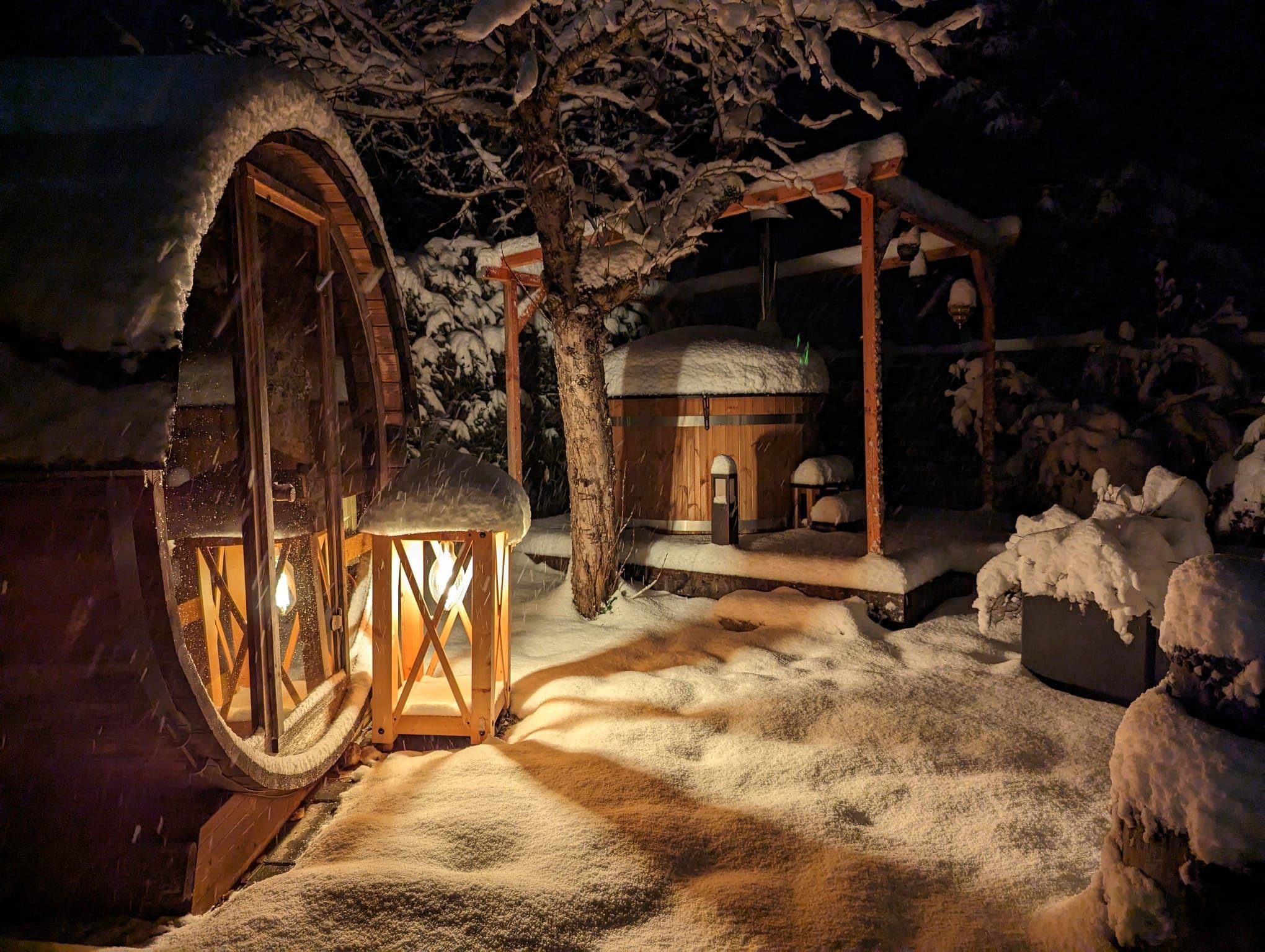 A snow-covered outdoor area with a wooden structure, a lantern, and a tree.