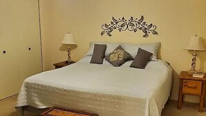 A neatly made bed with a white bedspread and three pillows, a small wooden chest, and two bedside tables with lamps. - Sunland Cottage in 55+ Golf Community (Mesa)
