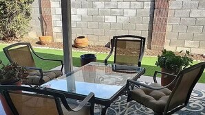 A glass-top table with four chairs, a patterned rug, and potted plants. - Sunland Cottage in 55+ Golf Community (Mesa)