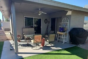 A covered patio area with outdoor furniture, a ceiling fan, and a grill.