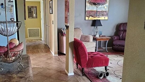 A living room with a red armchair, a beige sofa, a small table with a lamp, and a purple leather chair. - Sunland Cottage in 55+ Golf Community (Mesa)