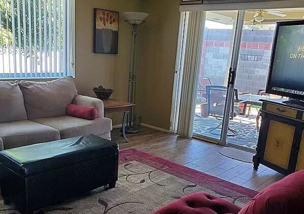 A living room with a sofa, a television, a floor lamp, and a sliding glass door leading to an outdoor area.