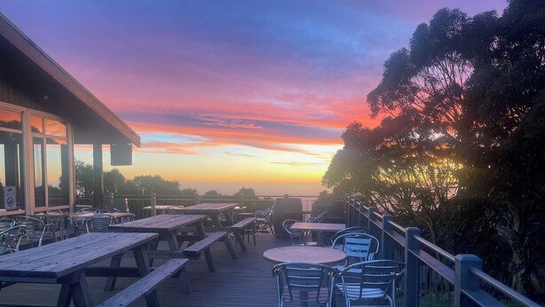 Eine Holzterrasse mit Picknicktischen und -stühlen mit Blick auf einen Sonnenuntergang.