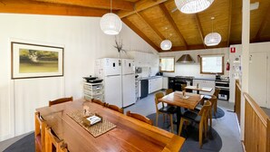 Eine moderne Küche mit weißen Geräten, ein Essbereich mit Holztisch und -stühlen sowie Pendelleuchten.