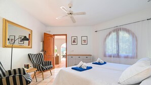 A hotel room with a bed, two chairs, a desk, a mirror, and a ceiling fan.