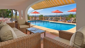 A poolside area with wicker furniture, red umbrellas, and a view of the mountains.