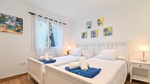 A hotel room with two beds, a large window with sheer curtains, and wall art.
