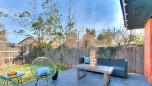 Un patio exterior con una mesa de madera, dos sillas de mimbre verde y un sofá gris.