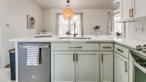 Una cocina moderna con armarios blancos, un refrigerador de acero inoxidable y una lámpara colgante.