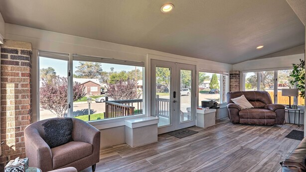 A spacious living room with a large sliding glass door leading to a deck, a brown leather sofa, and a white bench. - Beautiful Restored Victorian Home (Pueblo)