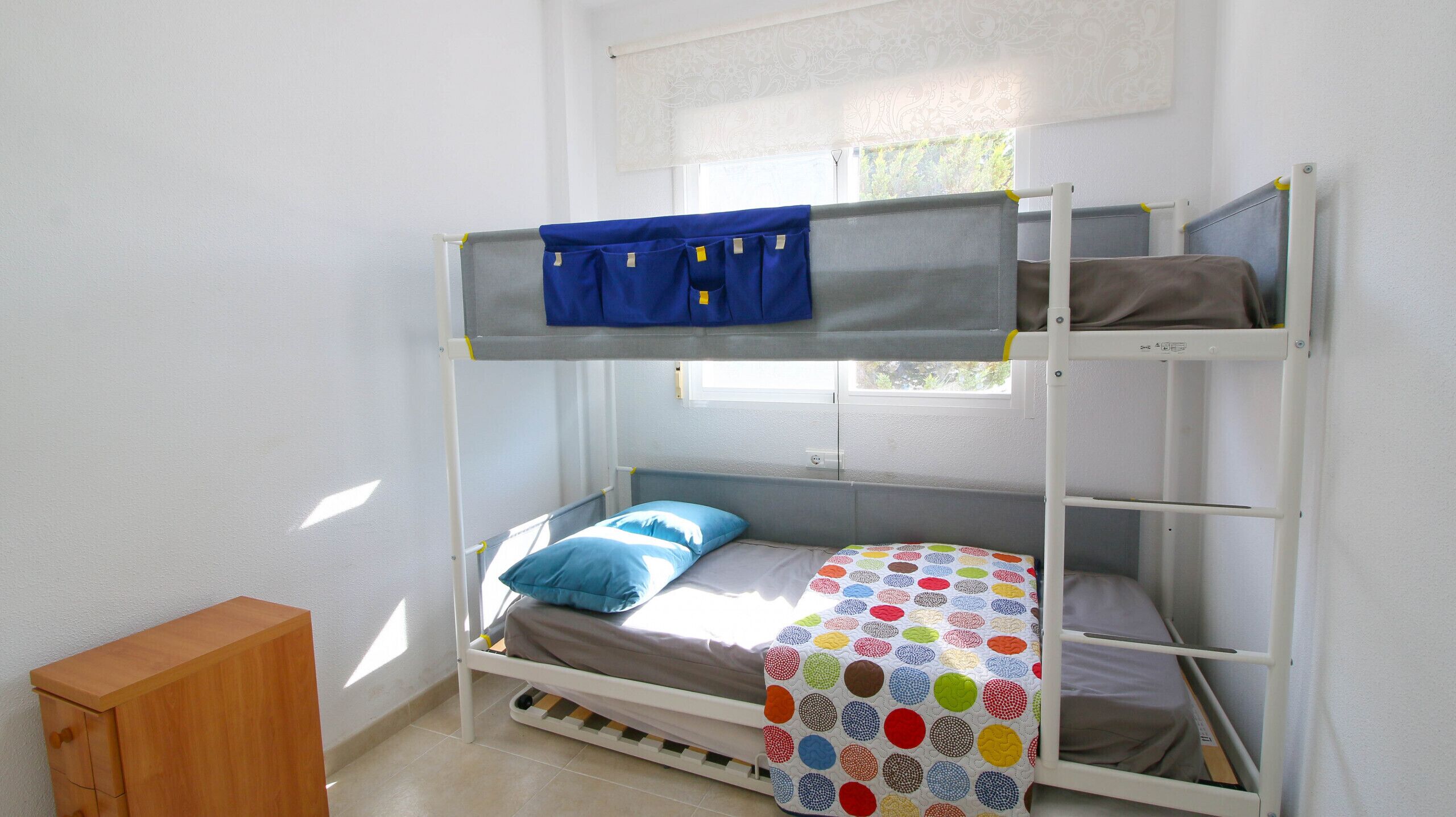 Un lit superposé avec un lit supérieur bleu et un lit inférieur recouvert d’une couette à pois colorés.