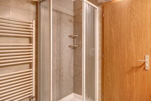 Une douche avec une porte en verre, une porte en bois sur la droite et un porte-serviettes blanc sur la gauche.